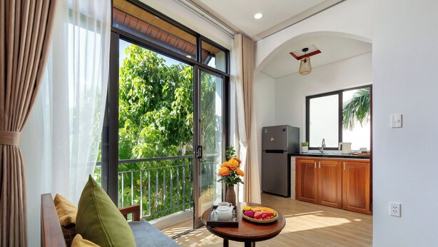 A modern living room with a sofa, a small table with a tray of fruit and flowers, and a view of a balcony with greenery. - Red Flower Cottages Homestay (Da Nang)