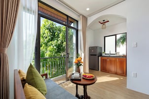 Una sala de estar moderna con un sofá, una mesita con una bandeja de frutas y flores, y vistas a un balcón con vegetación.