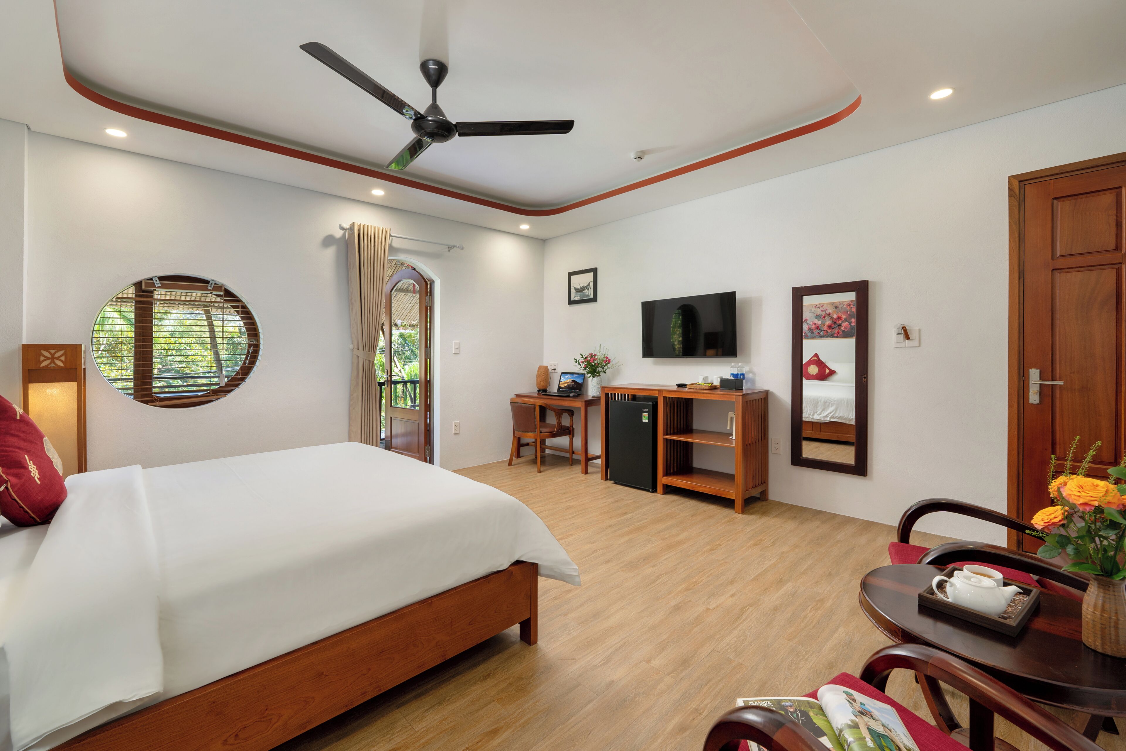 A hotel room with a bed, desk, chair, TV, and a dining table with a vase of flowers.
