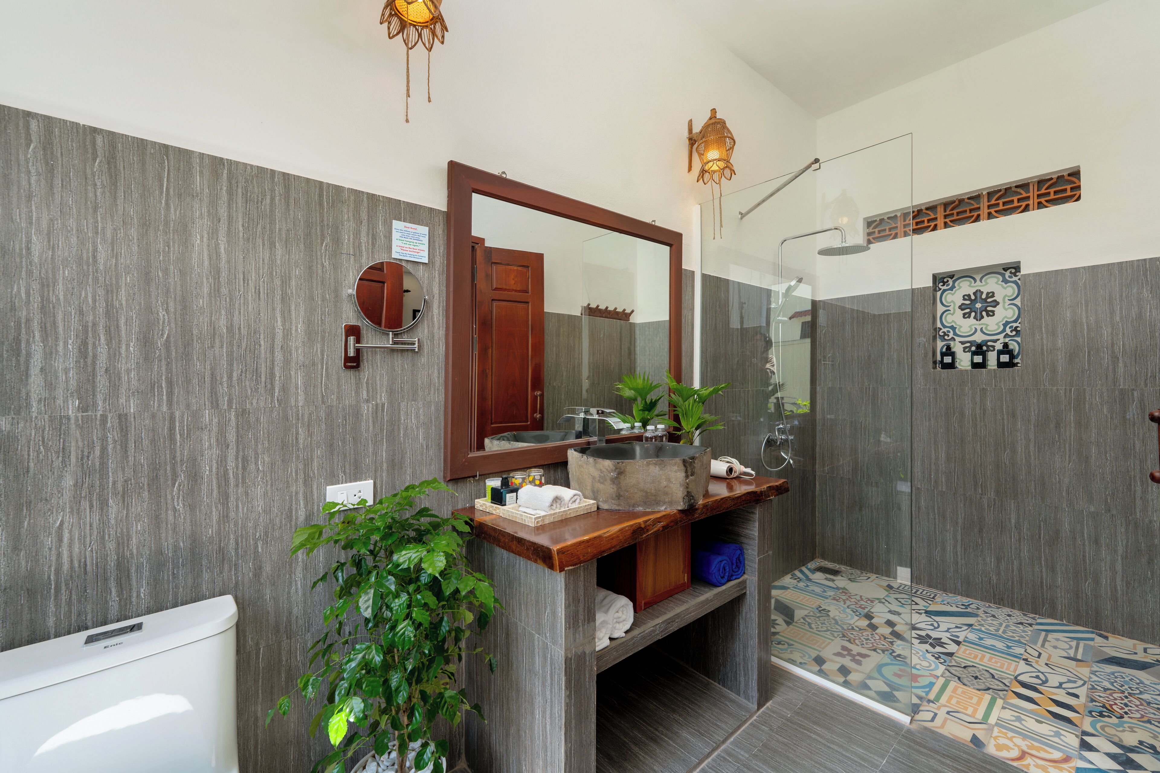 A modern bathroom with a wooden vanity, a large mirror, a shower with a glass door, and a patterned floor.