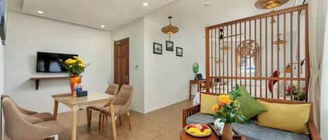 Una sala de estar moderna con un sofá de madera, una mesa de comedor de vidrio y un televisor montado en la pared.
