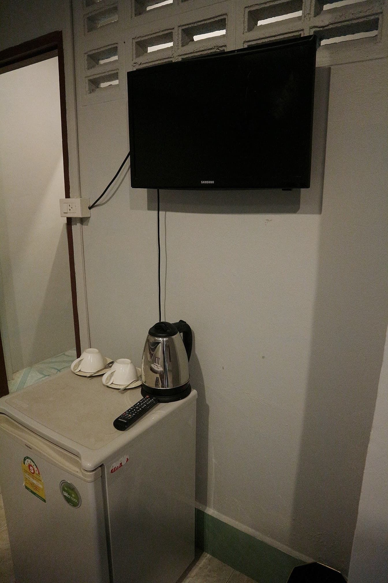 A small kitchenette with a refrigerator, a kettle, and a remote control.