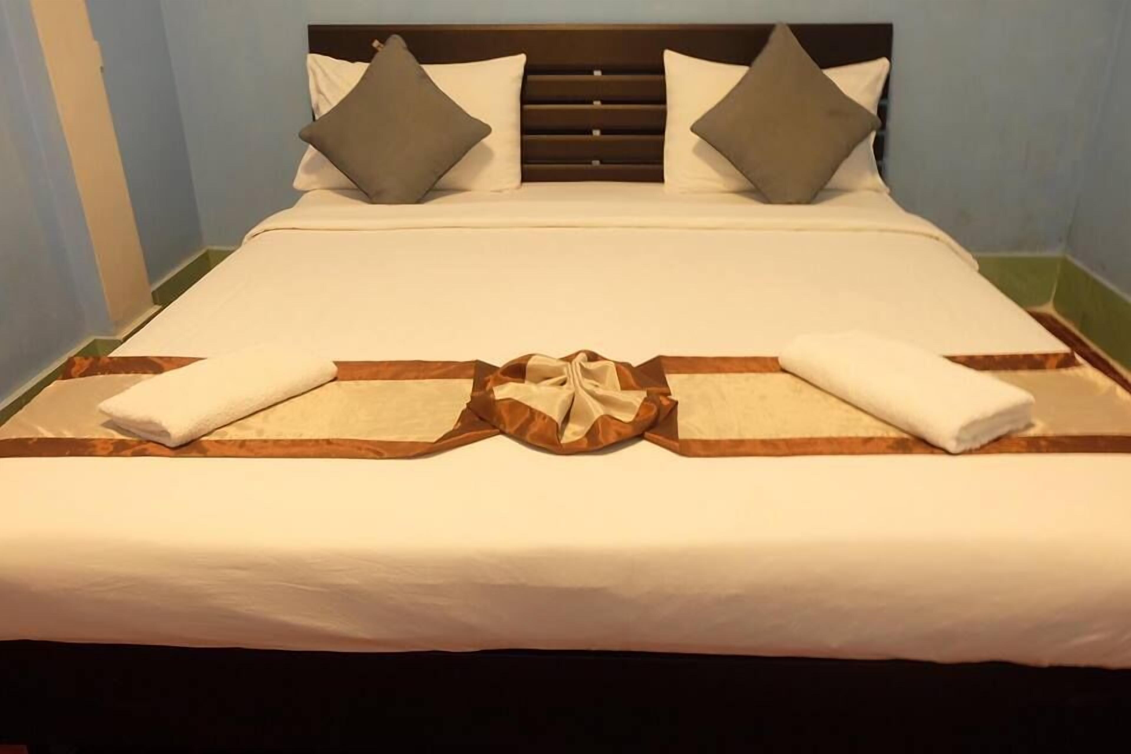 Uma cama bem arrumada com cabeceira de madeira, roupa de cama branca e duas toalhas dobradas ao pé da cama.