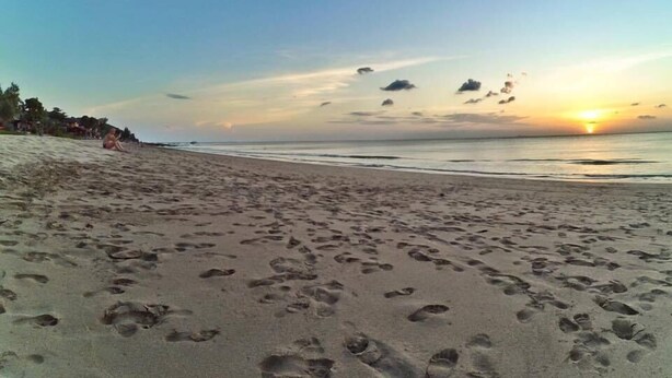Een strand met voetafdrukken in het zand en een zonsondergang op de achtergrond.