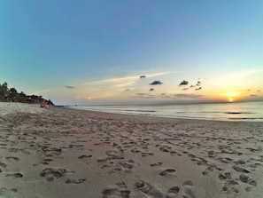 Uma praia com pegadas na areia e um pôr do sol ao fundo.
