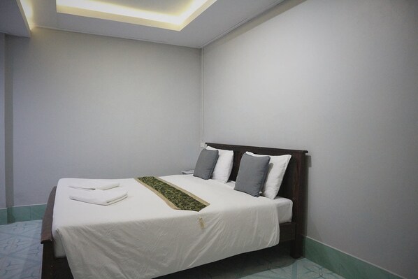 A neatly made bed with white linens and a green decorative throw, a wooden headboard, and a light-colored wall with a recessed ceiling light. - Marina Hut Guest House (Ko Lanta)