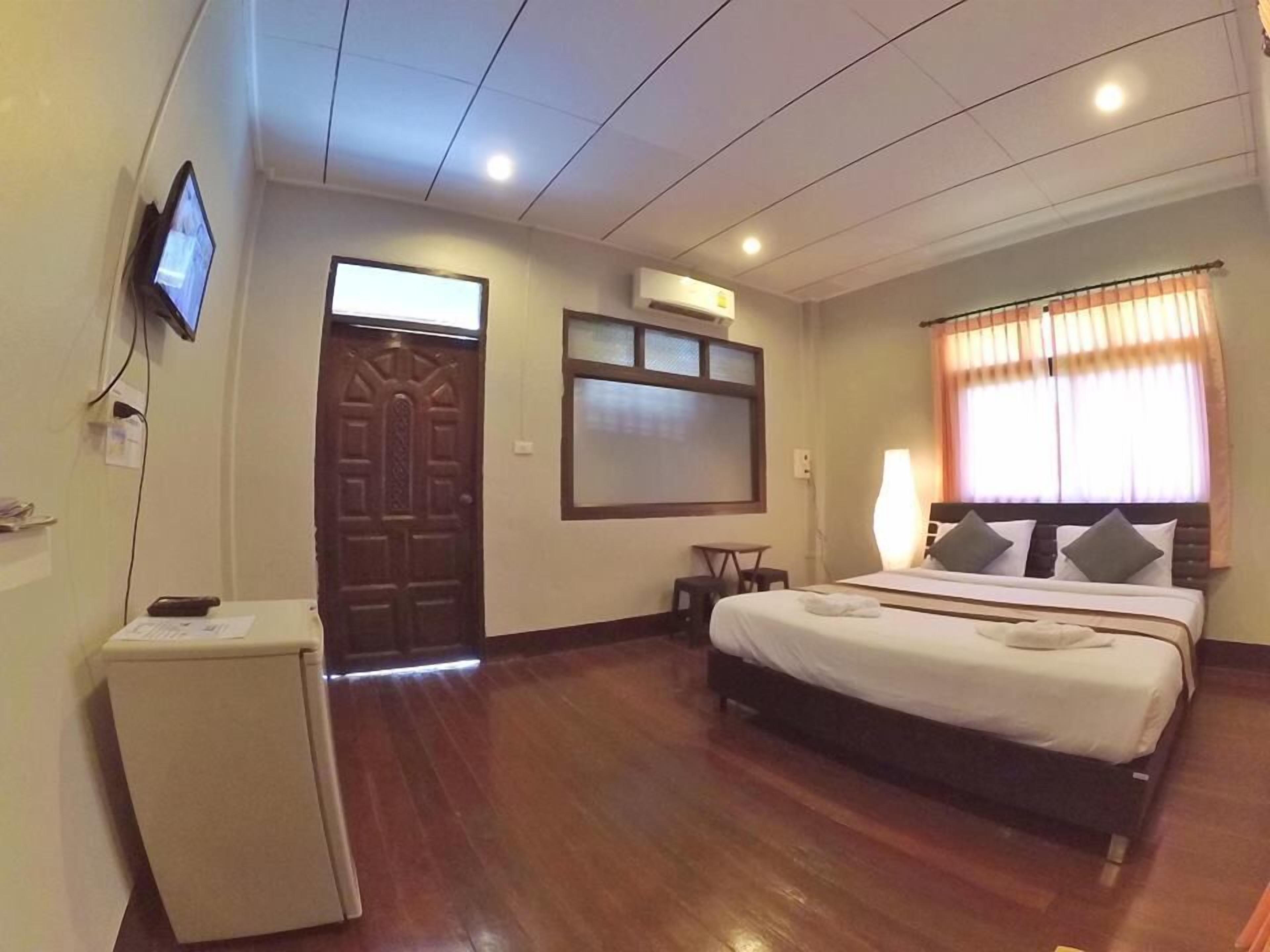 Quarto de hotel com cama, escrivaninha, televisão e janela com cortinas.