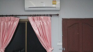 Een kamer met een raam, bedekt met roze gordijnen, een bruine deur en een airconditioningsunit aan de muur.