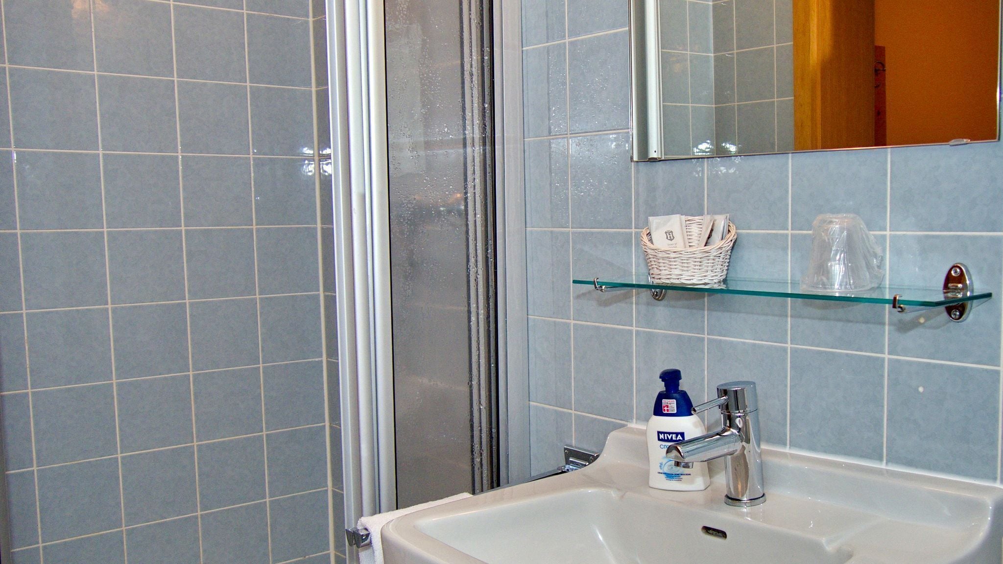 A bathroom with a glass shower enclosure, a sink with a chrome faucet, and a mirror above the sink.