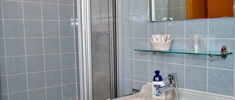 A bathroom with a glass shower enclosure, a sink with a chrome faucet, and a mirror above the sink.