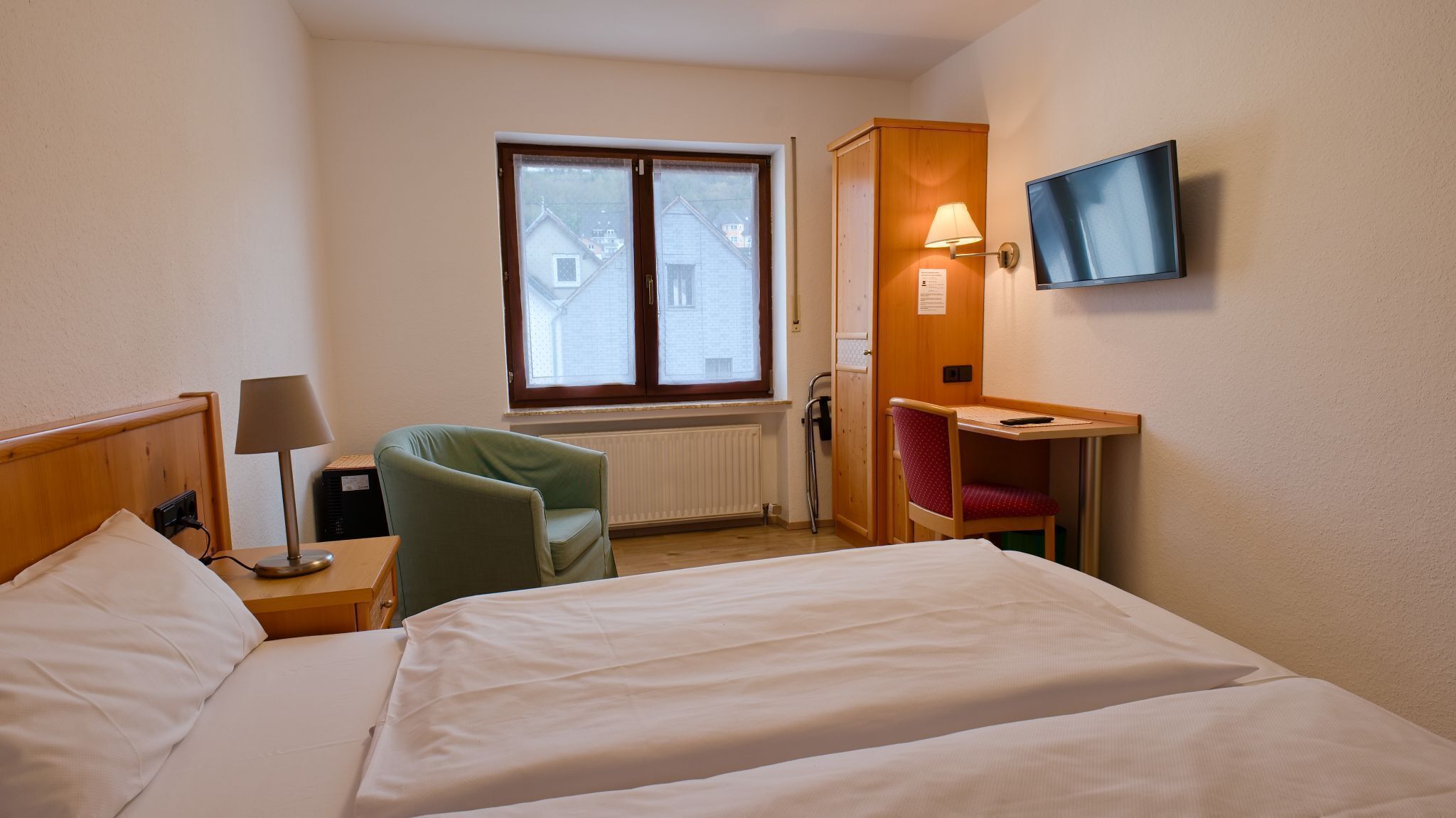 A hotel room with a bed, a desk, a chair, a TV, and a window.