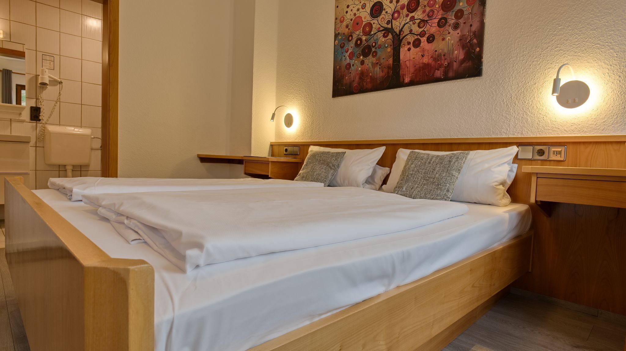 Un lit double avec une tête de lit et un pied de lit en bois, deux tables de chevet avec des lampes, un tableau accroché au mur et un mur recouvert de carreaux.
