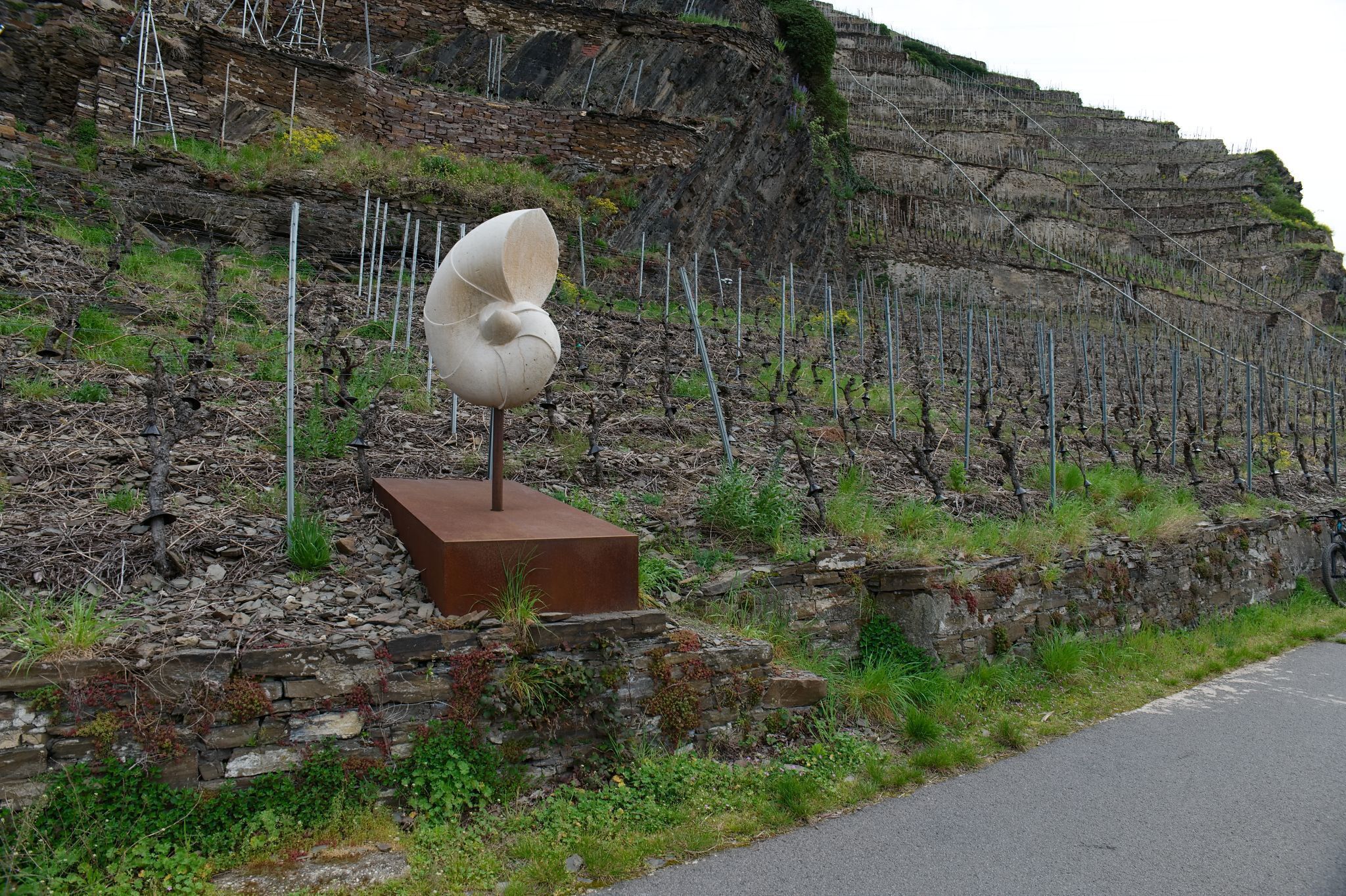 Una scultura su un piedistallo vicino a un pendio roccioso, con una strada in primo piano.