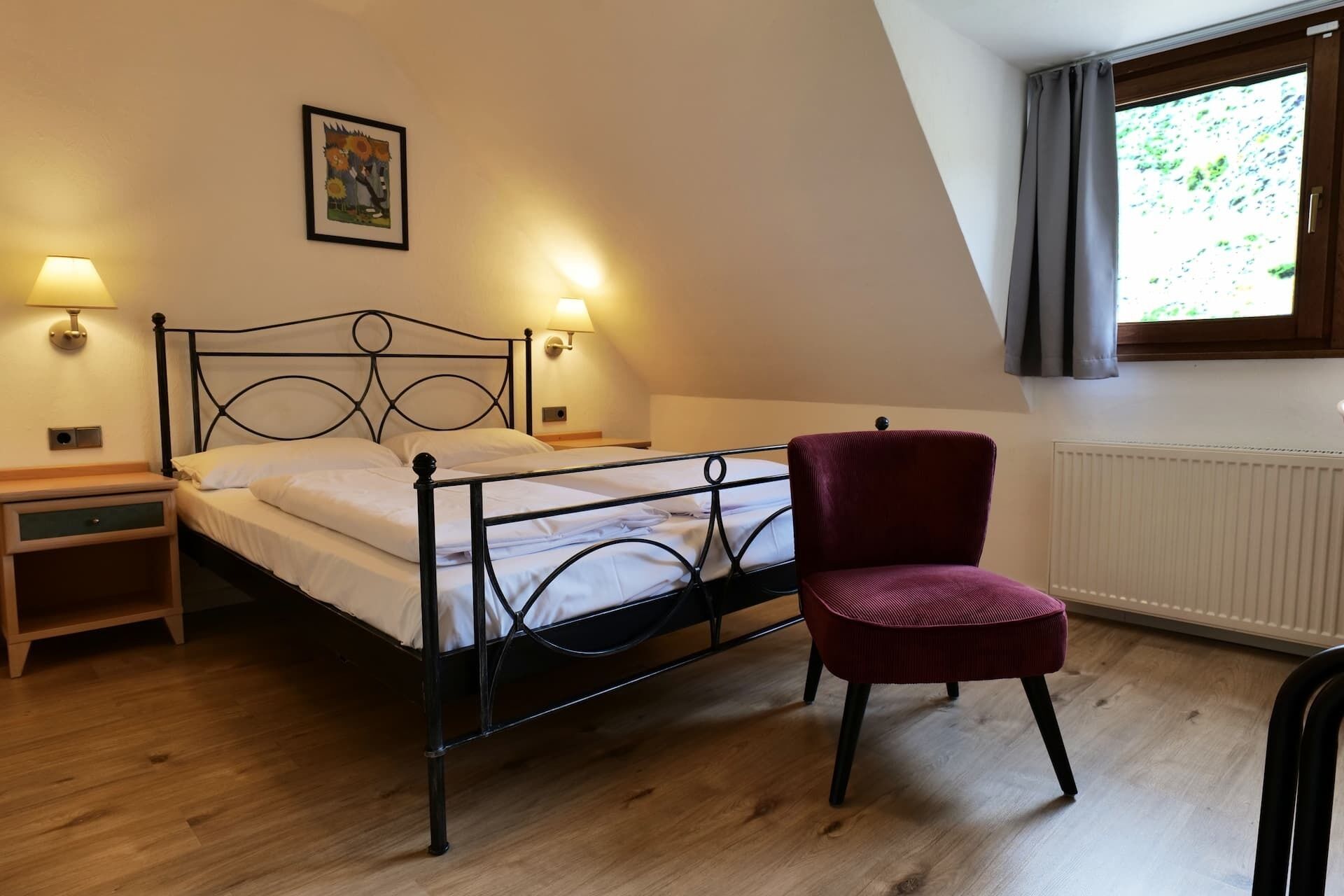 Quarto com cama, duas luminárias de cabeceira, uma cadeira, radiador e janela com cortinas.