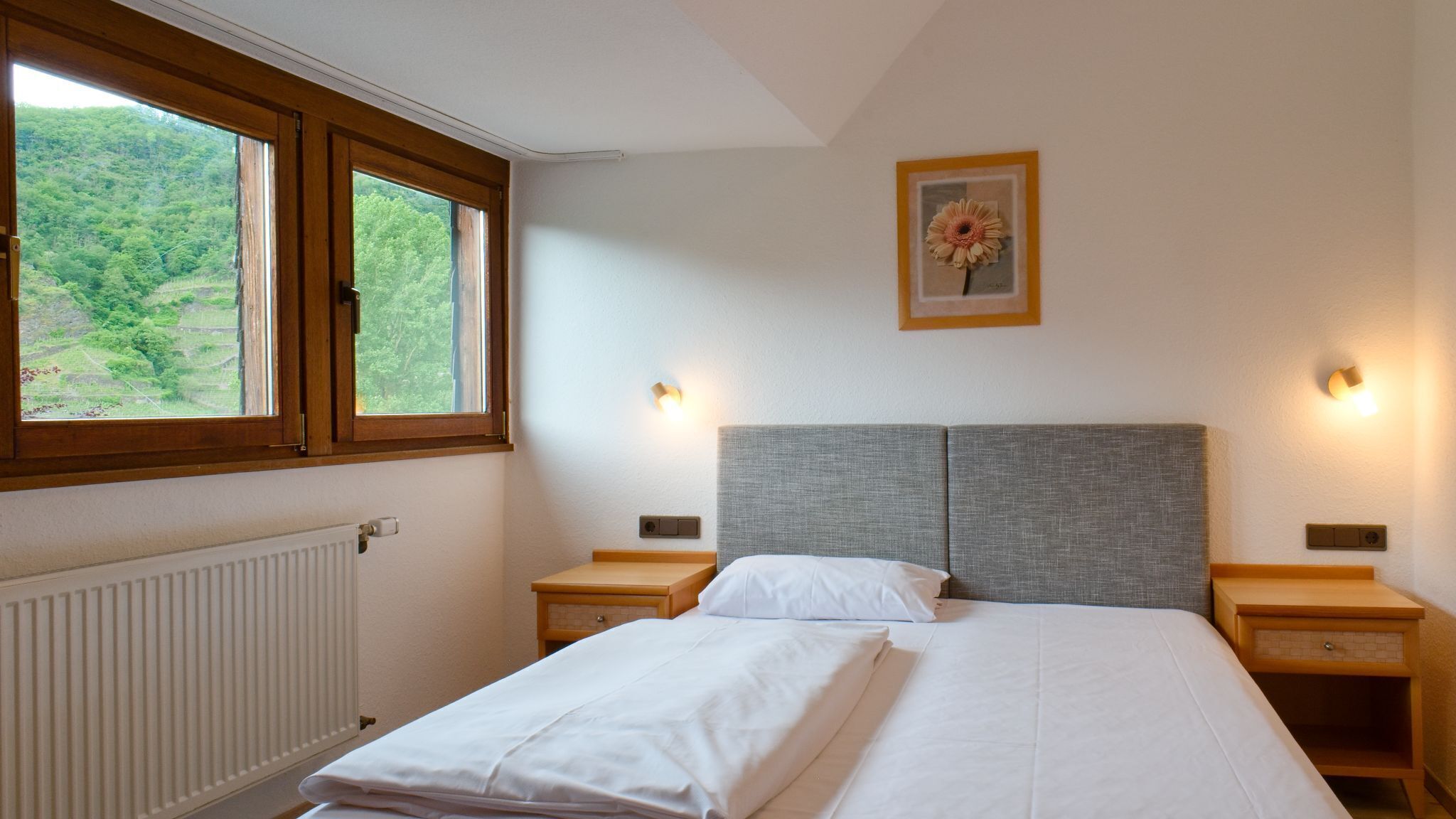 Un dormitorio con un ventanal grande, una cama con ropa de cama blanca, dos mesitas de noche y una lámpara de pared.