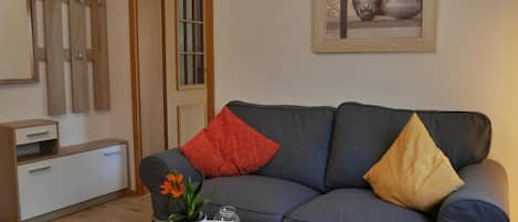 A living room with a grey sofa, a small table with a plant, a remote control, and a white cabinet.