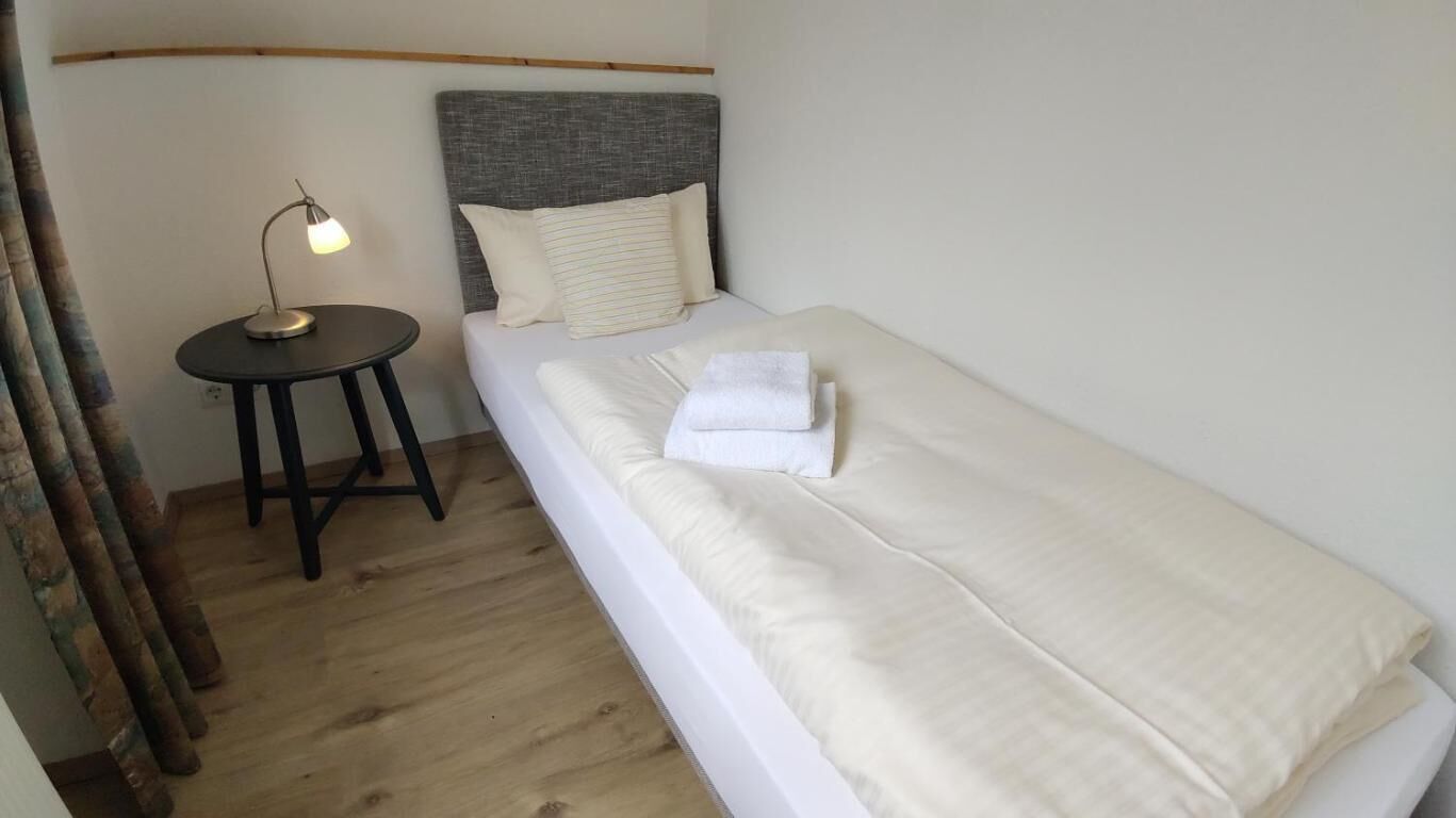 A single bed with a grey headboard, a bedside table with a lamp, and a wooden floor.