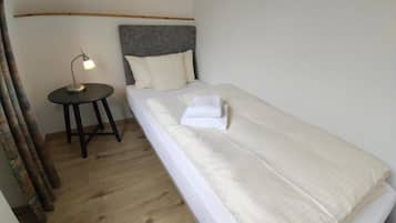 A single bed with a grey headboard, a bedside table with a lamp, and a wooden floor.