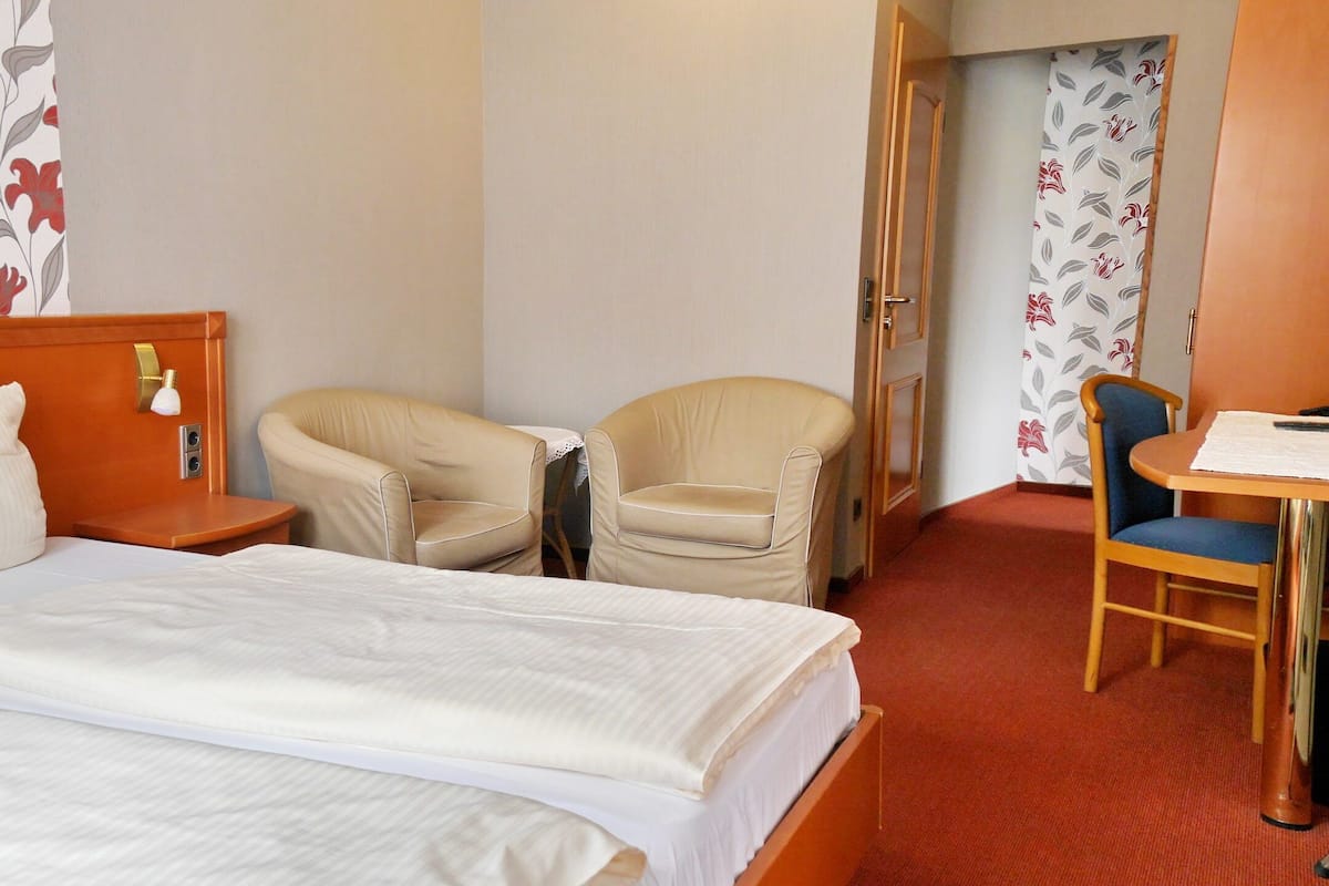 Een hotelkamer met een bed, twee stoelen, een tafeltje en een deur naar een andere kamer.