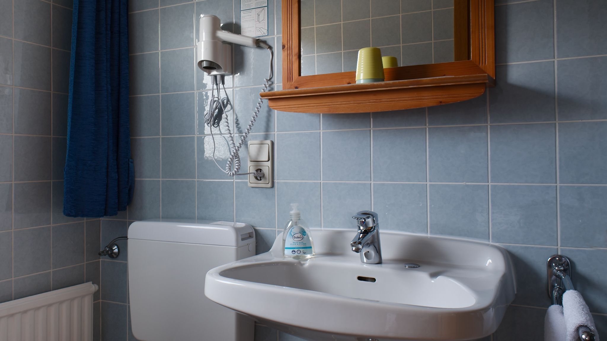 A bathroom with a white toilet, a sink with a mirror above it, and a blue towel hanging on the wall.