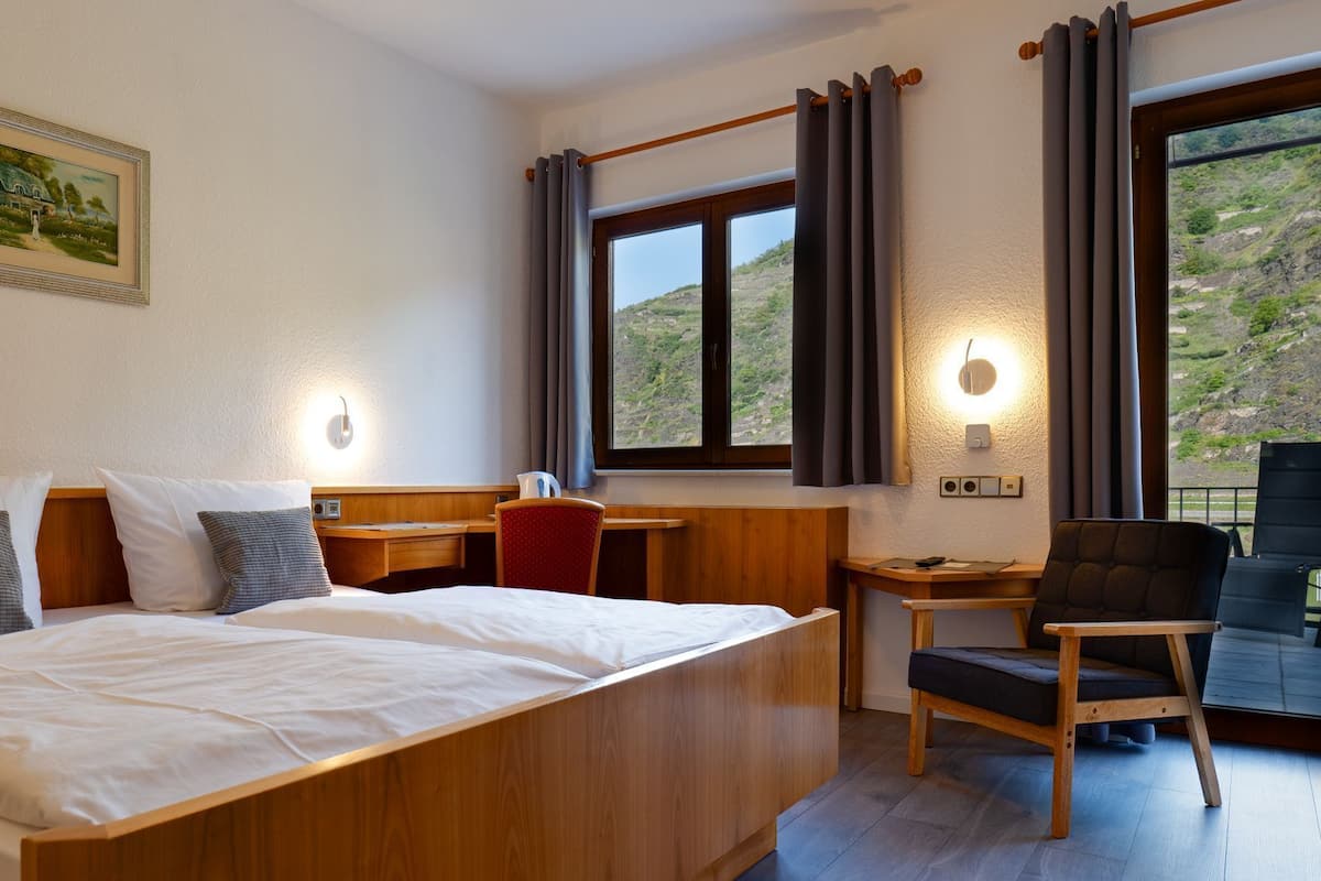 Een hotelkamer met een bed, een bureau, een stoel, een raam met gordijnen, een wandlamp en een ingelijste foto.