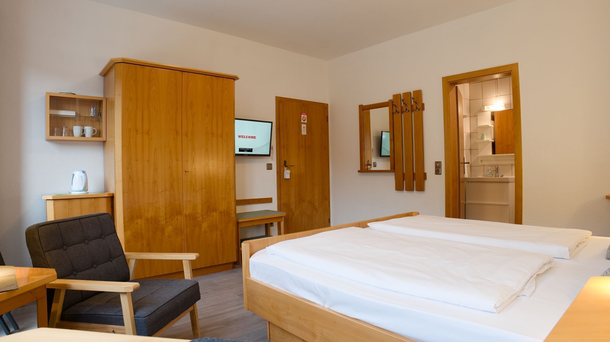 Quarto de hotel com uma cama, escrivaninha, cadeira, armário e televisão.