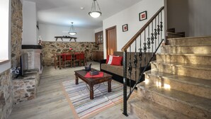 A spacious living area with a stone fireplace, wooden staircase, and a dining area with a table and chairs.