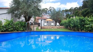A swimming pool with a clear blue water surface, surrounded by a stone wall and lush greenery.