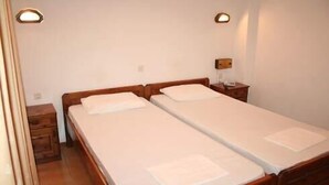 A double bed with a wooden headboard, a nightstand, and a wall-mounted lamp. - Hotel Vicky (Thasos)