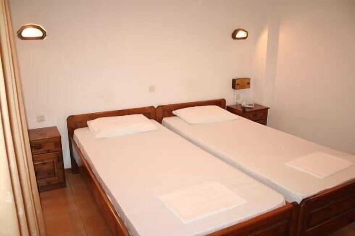 A double bed with a wooden headboard, a nightstand, and a wall-mounted lamp.
