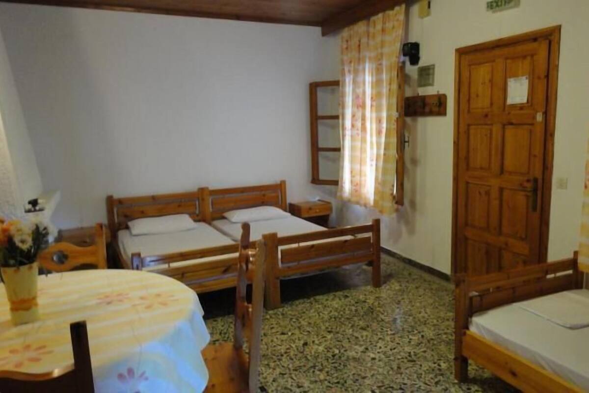 A room with two wooden beds, a small table with a floral tablecloth, and a wooden wardrobe.