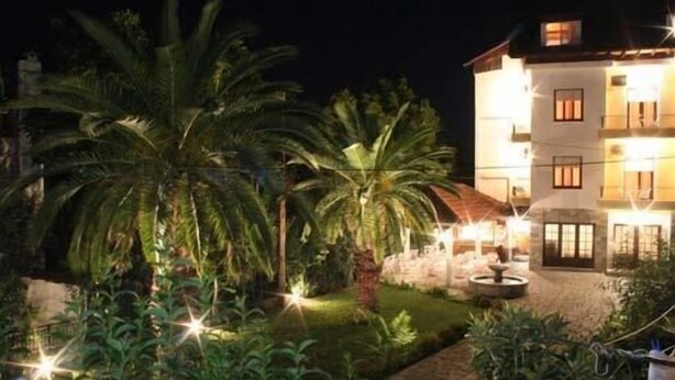 A multi-story building with a well-lit exterior and a landscaped garden with palm trees. - Hotel Vicky (Thasos)