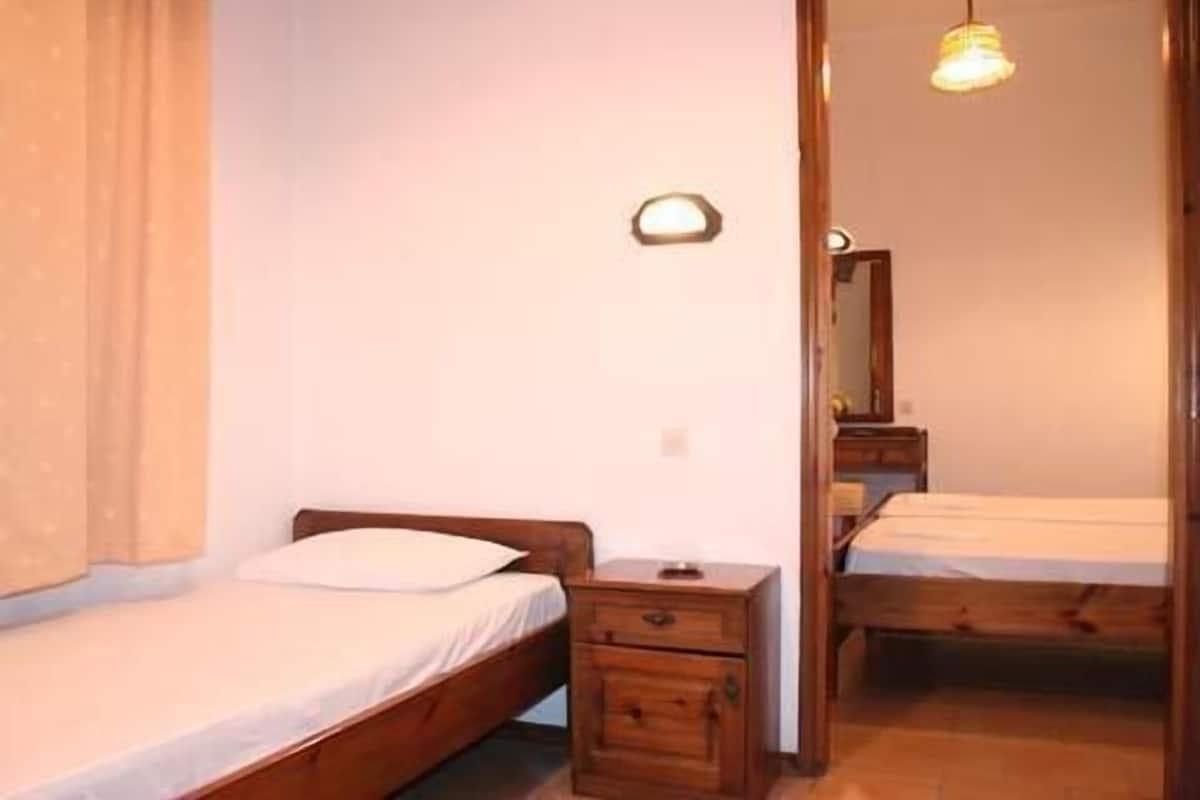 A small, simple room with two wooden beds, a nightstand, and a mirror.