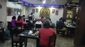 A restaurant with tables and chairs, a Buddha statue on the wall, and people dining. - Hotel Kathmandu Home Annex (Kathmandu)