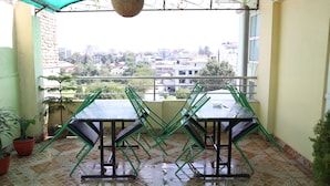 A balcony with a tiled floor, two tables, and green chairs. - Hotel Kathmandu Home Annex (Kathmandu)