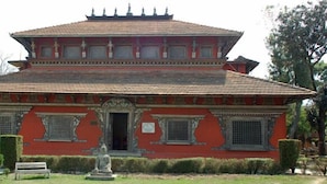 A traditional building with a red facade, a tiled roof, and a statue in front. - Hotel Kathmandu Home Annex (Kathmandu)
