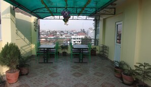 Un balcón con vistas a un paisaje urbano, que incluye una mesa, sillas, plantas en macetas y un farol colgante.