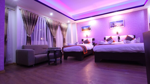 A hotel room with a sofa, two beds, a small table, and a wall-mounted TV. - Hotel Kathmandu Home Annex (Kathmandu)