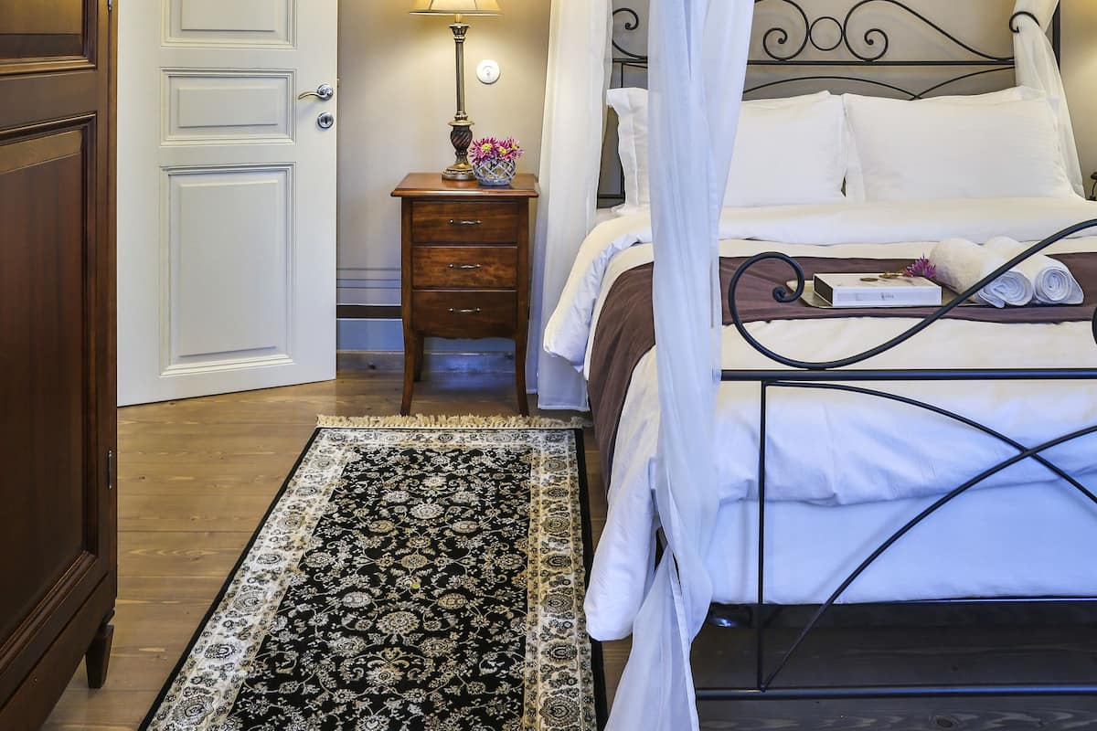 A bedroom with a four-poster bed, a bedside table with a lamp, and a decorative rug.