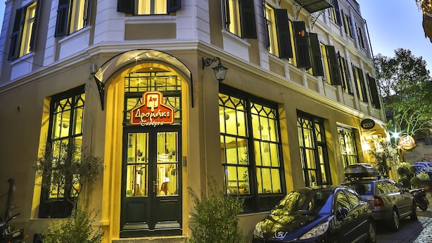 A corner building with a sign indicating a restaurant, a balcony, and parked cars. - 1905 Boutique Hotel (Xanthi)