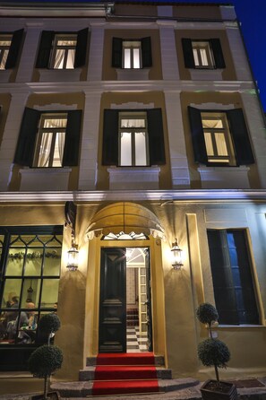 A building with a red carpet leading to a staircase, a black door, and two small potted trees. - 1905 Boutique Hotel (Xanthi)