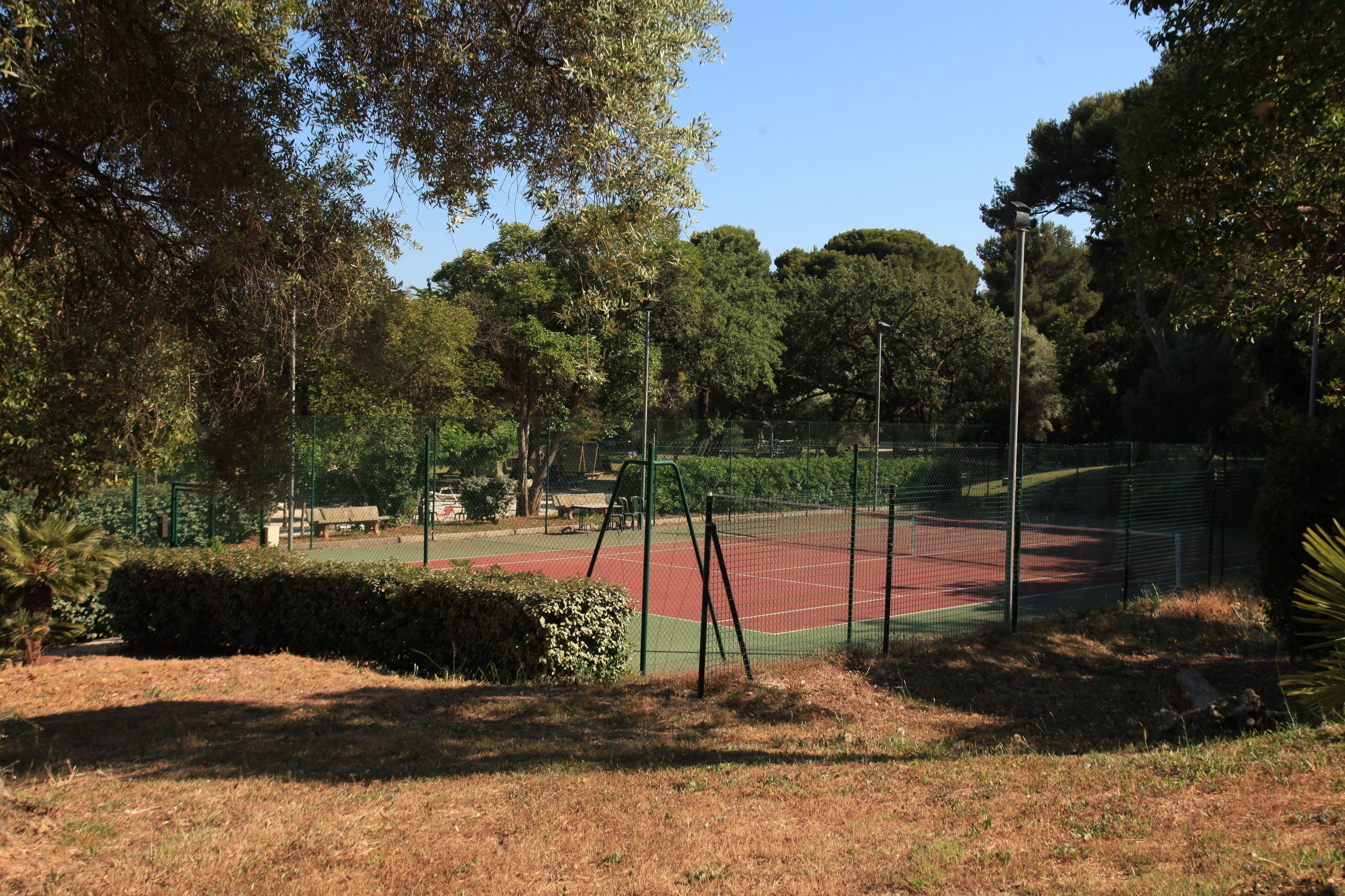 A tennis court surrounded by trees and a fence.