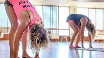 A yoga class in a well-lit room with large windows, a wooden floor, and exercise mats.