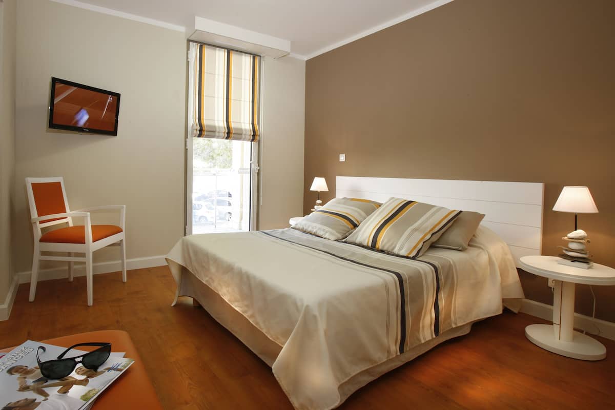 A bedroom with a bed, a chair, a TV, and a window with curtains.