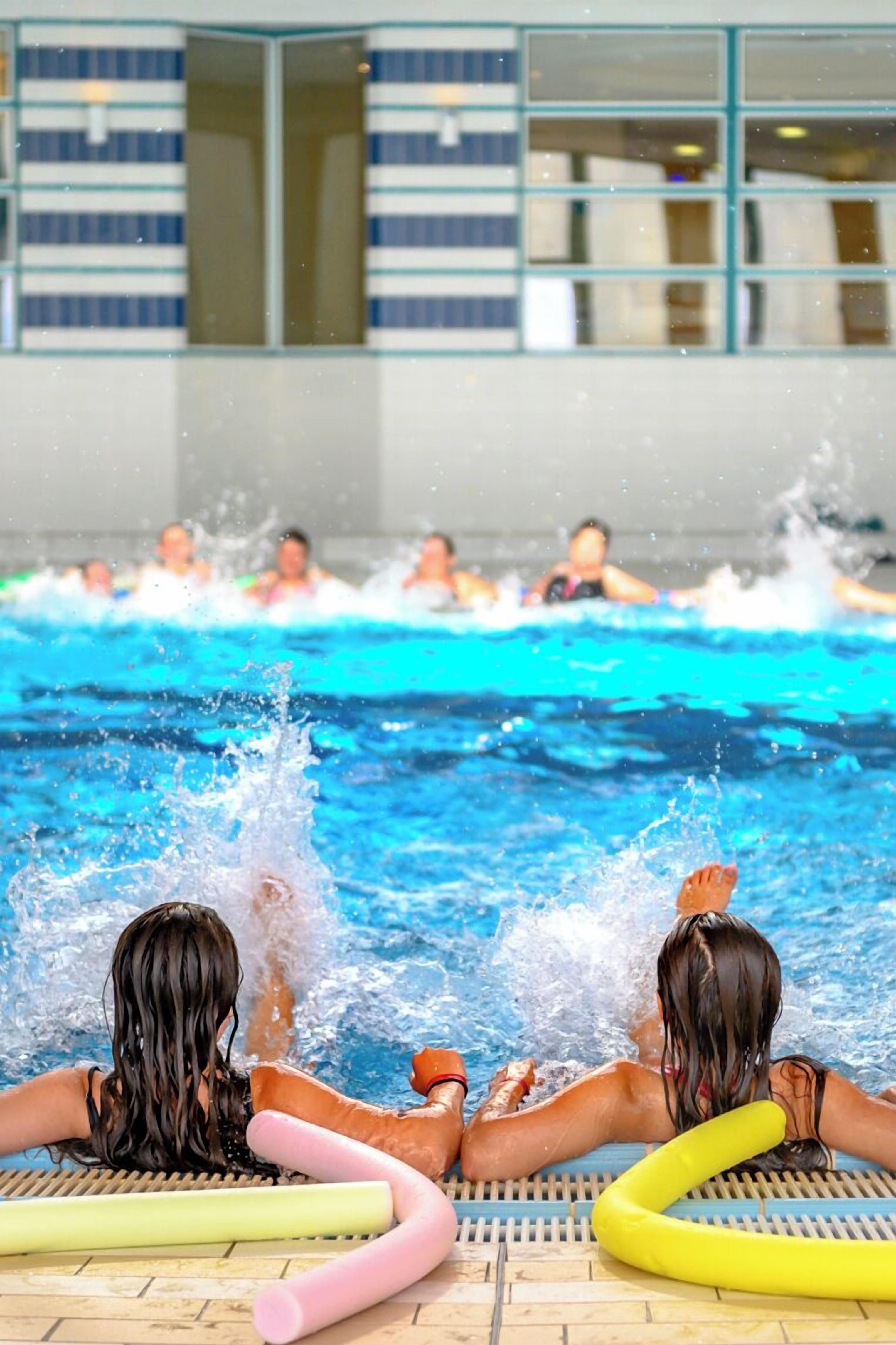A pool area with people swimming and splashing water.