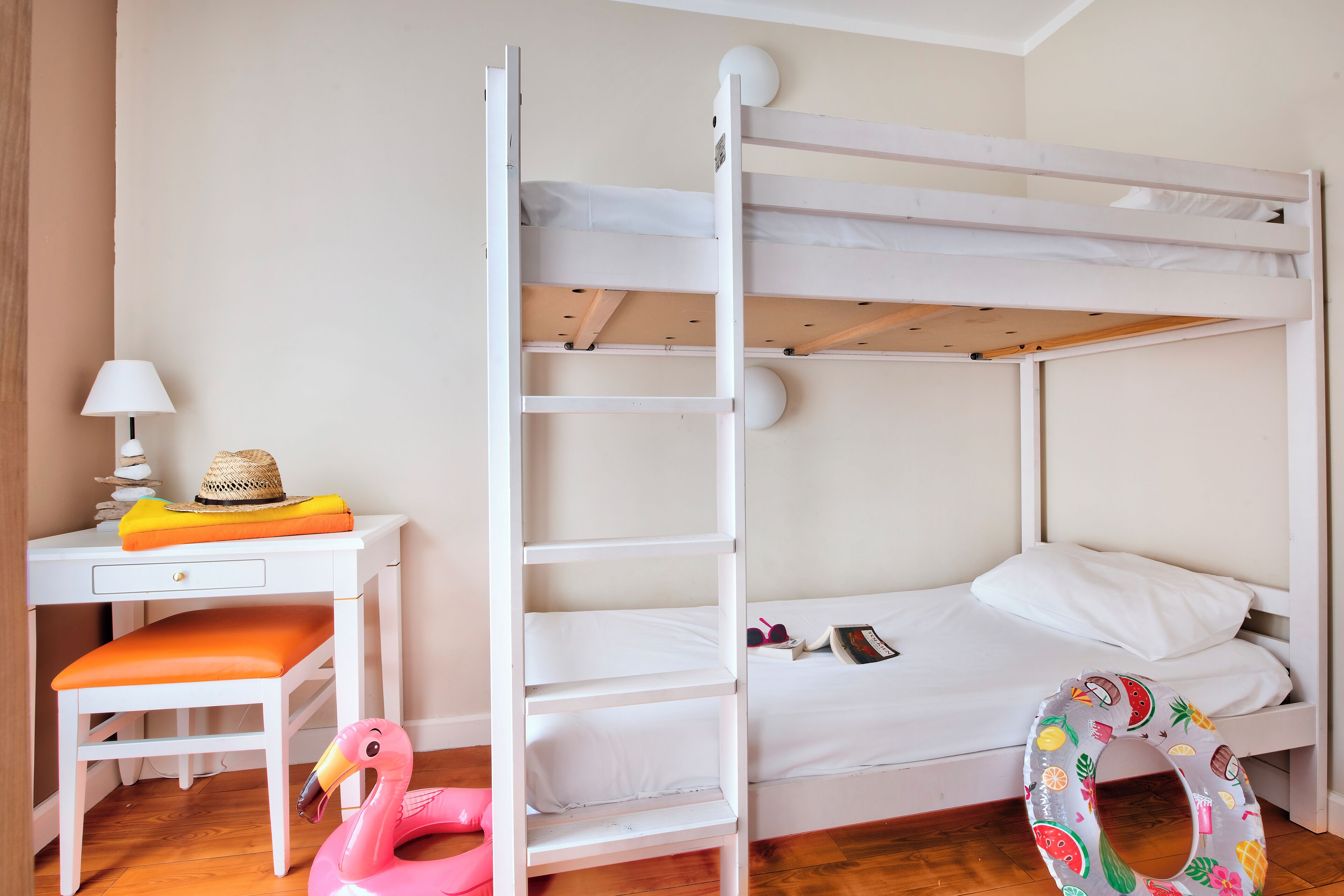 Een stapelbed met een ladder, een bureau met een lamp, een stoel en een flamingo drijvend speelgoed.