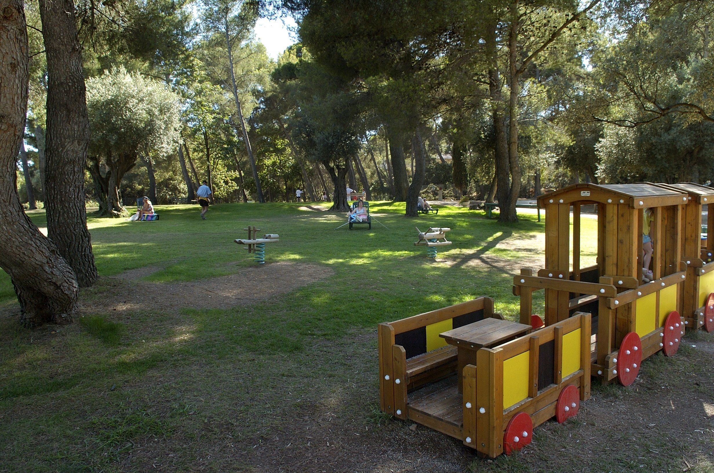 A park with a wooden play structure, picnic tables, and benches.