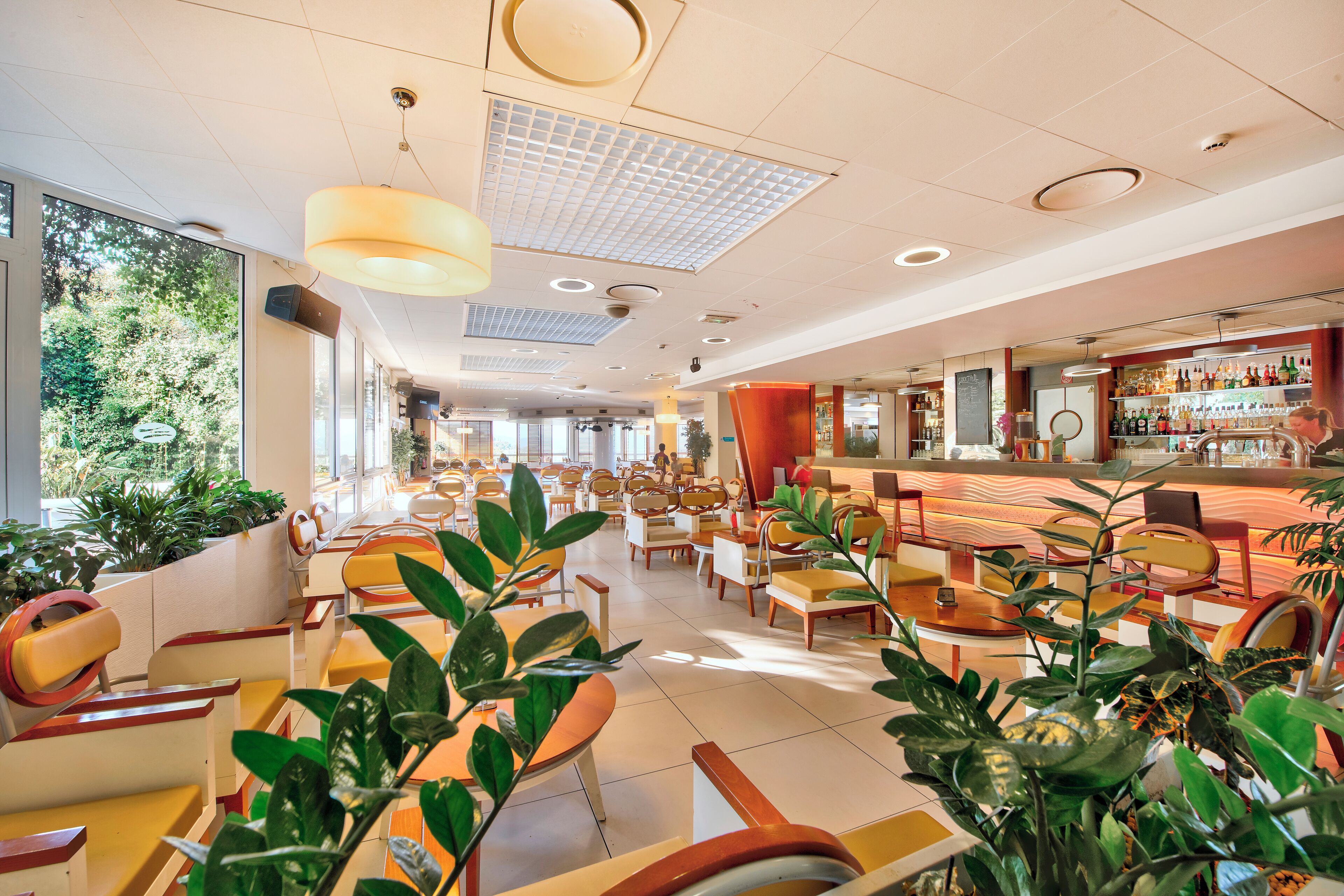 Un vaste espace intérieur aménagé avec différents types de sièges, notamment des tables et des chaises, ainsi qu’un bar doté d’étagères remplies de bouteilles.