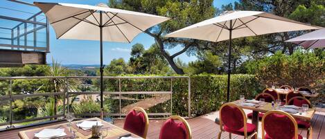 An outdoor dining area with tables and chairs, large umbrellas, and a scenic view.