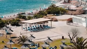 Un hôtel situé sur la côte, avec des espaces de détente en bord de plage, des parasols et une vue sur la mer et les collines.